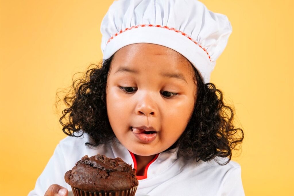 Petite fille en tenue de chef avec un muffin au chocolat