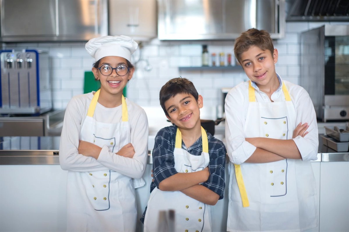 Trois enfants souriants en tablier dans une cuisine